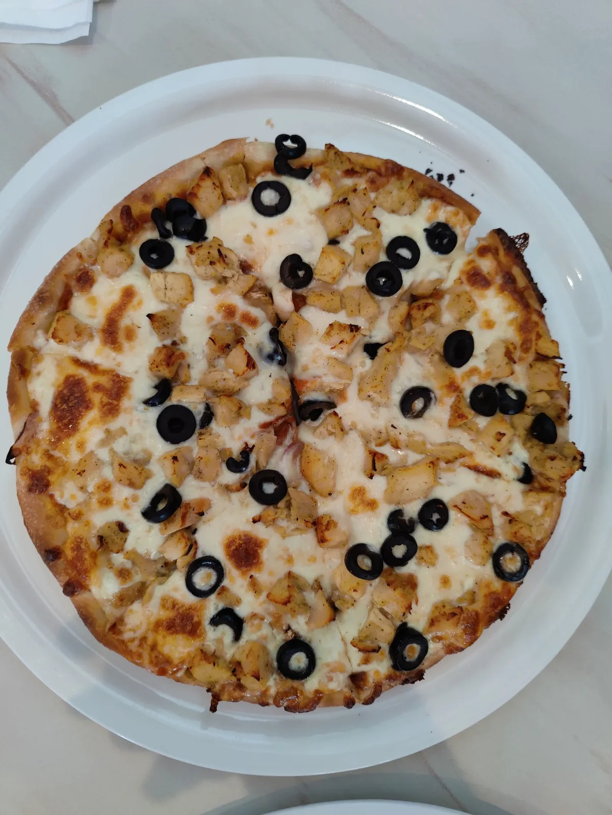 Nybakad pizza skuren i bitar med kyckling och oliver